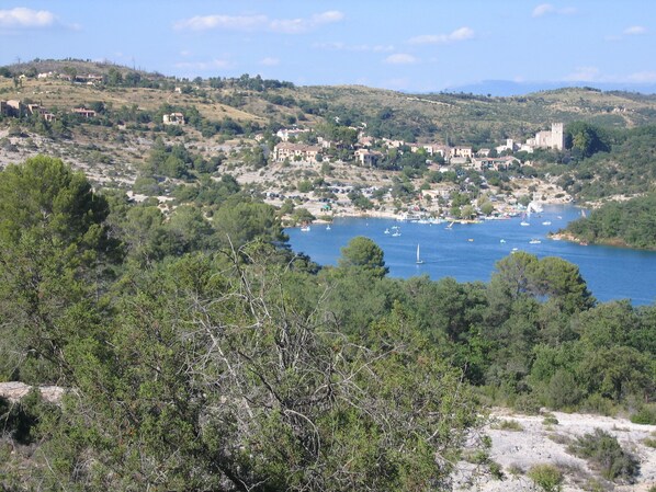 A coastal town with buildings along the shoreline, a clear blue sea, and surrounding hills.