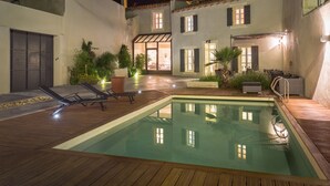 A swimming pool with two lounge chairs, a wooden deck, and a building with multiple windows and doors. - Quiet home in the heart of the Alpilles with private pool (Eyragues)