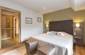 Een slaapkamer met een groot bed, twee bedlampen, een houten deur en een klein bankje.