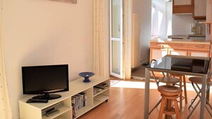 A modern living room with a flat-screen TV, bookshelves, a dining area with stools, and a kitchen in the background. - Bright apartment for 2, Trébeurden center, near beach, pets allowed (Trébeurden)