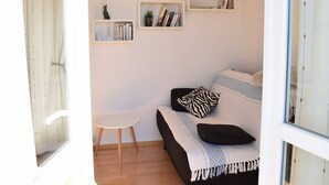 A modern living room with a sofa, a small white table, and two wall-mounted shelves with books and decorative items. - Bright apartment for 2, Trébeurden center, near beach, pets allowed (Trébeurden)
