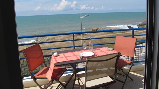 A table with two chairs and a bottle of water, overlooking a beach with a rocky shoreline and the ocean. - T2 apartment wonderful sea view, WLAN available garage 2 bicycles available  (Saint-Hilaire-De-Riez)