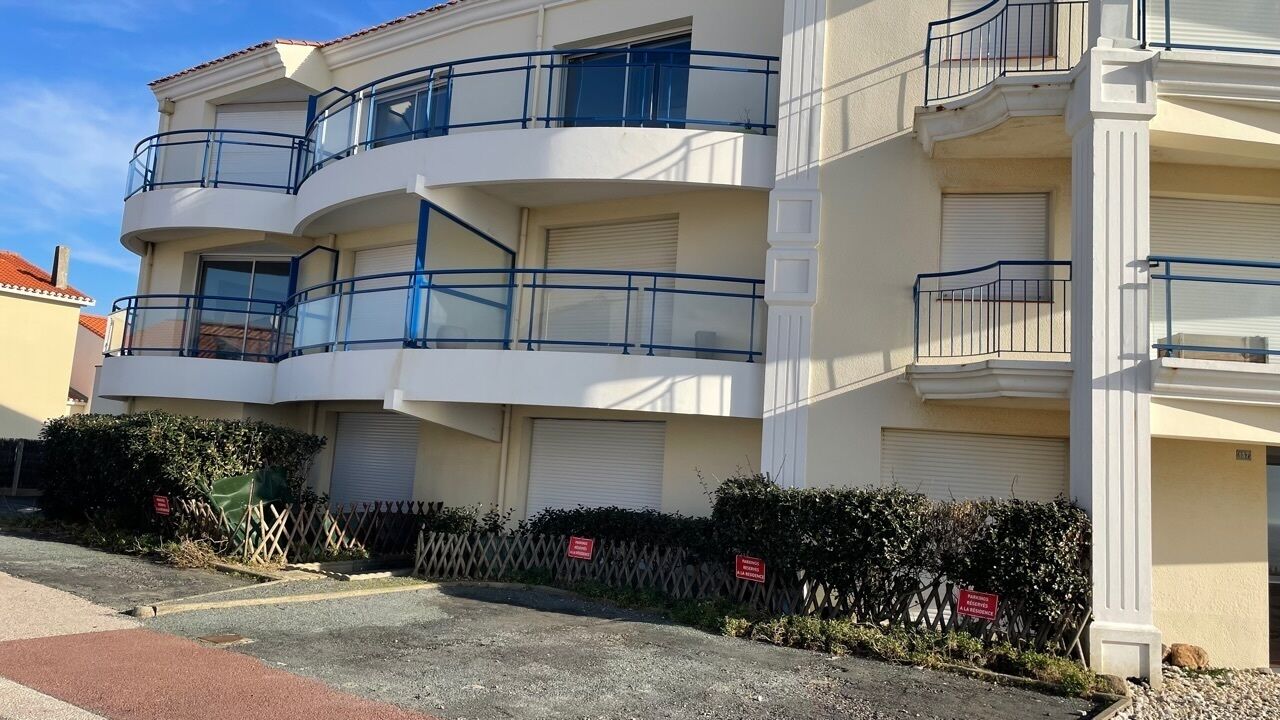 Un edificio residencial de varios pisos con balcones, una entrada protegida por una reja y cielo despejado.
