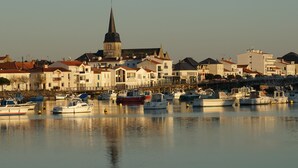 A harbor with boats docked, a prominent church with a tall spire, and a row of buildings with balconies. - T2 apartment wonderful sea view, WLAN available garage 2 bicycles available  (Saint-Hilaire-De-Riez)