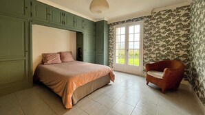 A bedroom with a bed, a chair, and a door leading to a balcony. - House with pool in the heart of the Castles of the Loire (Cour-Cheverny)