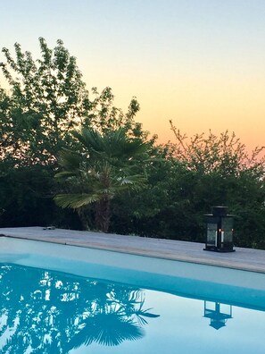 A swimming pool with a clear reflection, surrounded by lush greenery and a sunset sky. - House with pool in the heart of the Castles of the Loire (Cour-Cheverny)