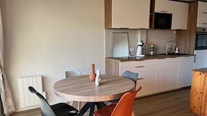 Een moderne keuken met witte kastjes, een magnetron en een koffiezetapparaat. Er staat een eettafel met twee stoelen.