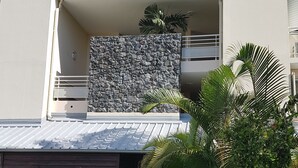 A modern two-story house with a stone facade, a garage, and a balcony with a view of the sky. - Magnificent and luxurious 4-star T2 with sea view, swimming pool and garden (Saint-Gilles-Les-Bains)