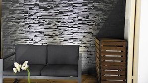 A room with a grey sofa, a wooden crate, and a textured wall. - Magnificent and luxurious 4-star T2 with sea view, swimming pool and garden (Saint-Gilles-Les-Bains)