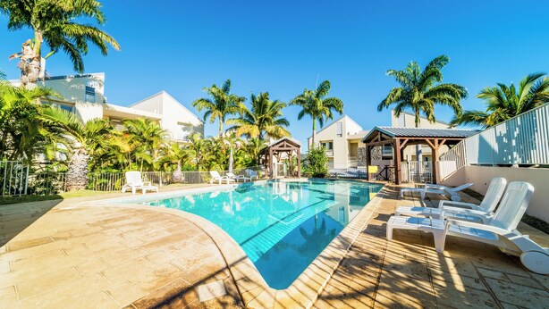 A swimming pool with lounge chairs, palm trees, and a clear blue sky. - Magnificent and luxurious 4-star T2 with sea view, swimming pool and garden (Saint-Gilles-Les-Bains)