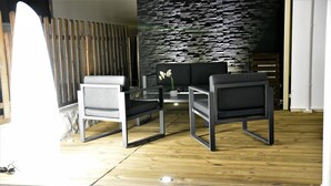 A modern room with a stone wall, two grey sofas, a small table, and a wooden floor. - Magnificent and luxurious 4-star T2 with sea view, swimming pool and garden (Saint-Gilles-Les-Bains)