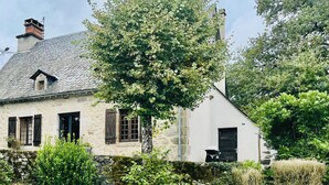 Ein Gebäude aus Stein mit einem Ziegeldach, ein Baum davor und ein Pool mit Liegestühlen.