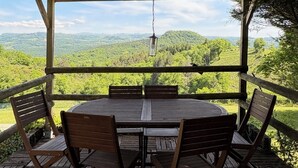 Eine Holzterrasse mit einem runden Tisch und Stühlen, mit Blick auf eine üppige, grüne Landschaft.