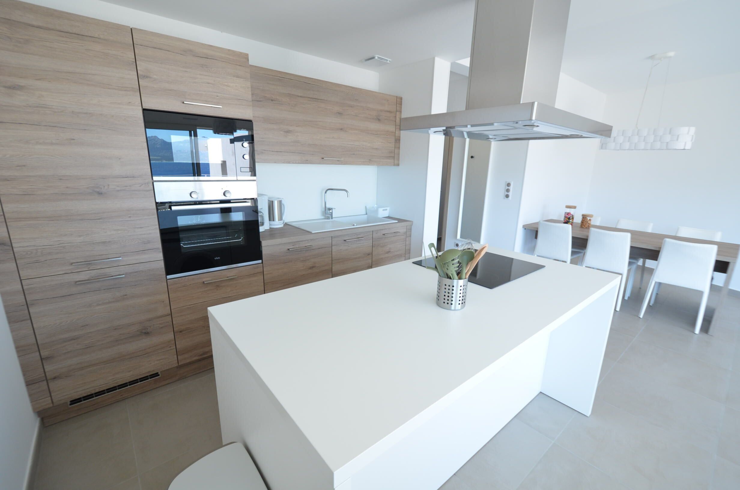 Une cuisine moderne avec des meubles en bois, un four encastré et un plan de travail blanc.