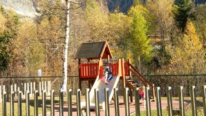 A playground with a slide and climbing area, surrounded by a wooden fence and trees.