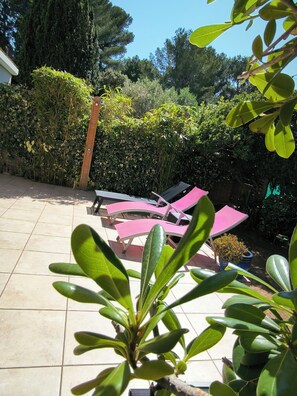 Eine Terrassenfläche mit gefliestem Boden, einer Holzupergola und mehreren Liegestühlen.