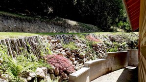 A landscaped garden with a stone retaining wall, a concrete pathway, and various plants including ferns and red foliage. - Chalet *** sleeps 6/8 on Lac de Pannecière, near Chaumard (Corancy)