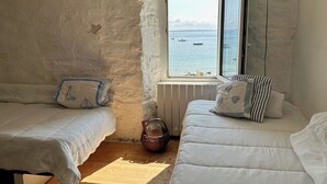 Una camera accogliente con due letti, vista sul mare e un rustico muro in pietra.