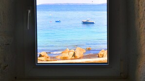 Una finestra con vista su un mare calmo e una costa rocciosa.