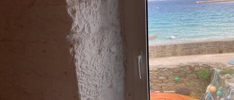 A room with a view of the sea through a window, a stone wall, and a small outdoor area with colorful decorations.