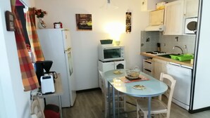 Eine kleine Küche mit Esstisch, Stühlen, Kühlschrank, Mikrowelle, Backofen und Spüle.