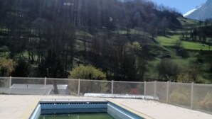 Ein Schwimmbecken mit gefliestem Sonnendeck, umgeben von einem Zaun, mit Blick auf eine hügelige Landschaft im Hintergrund.
