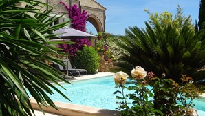 Et poolområde med en klar, blå pool omgivet af frodigt grønt og blomstrende planter.
