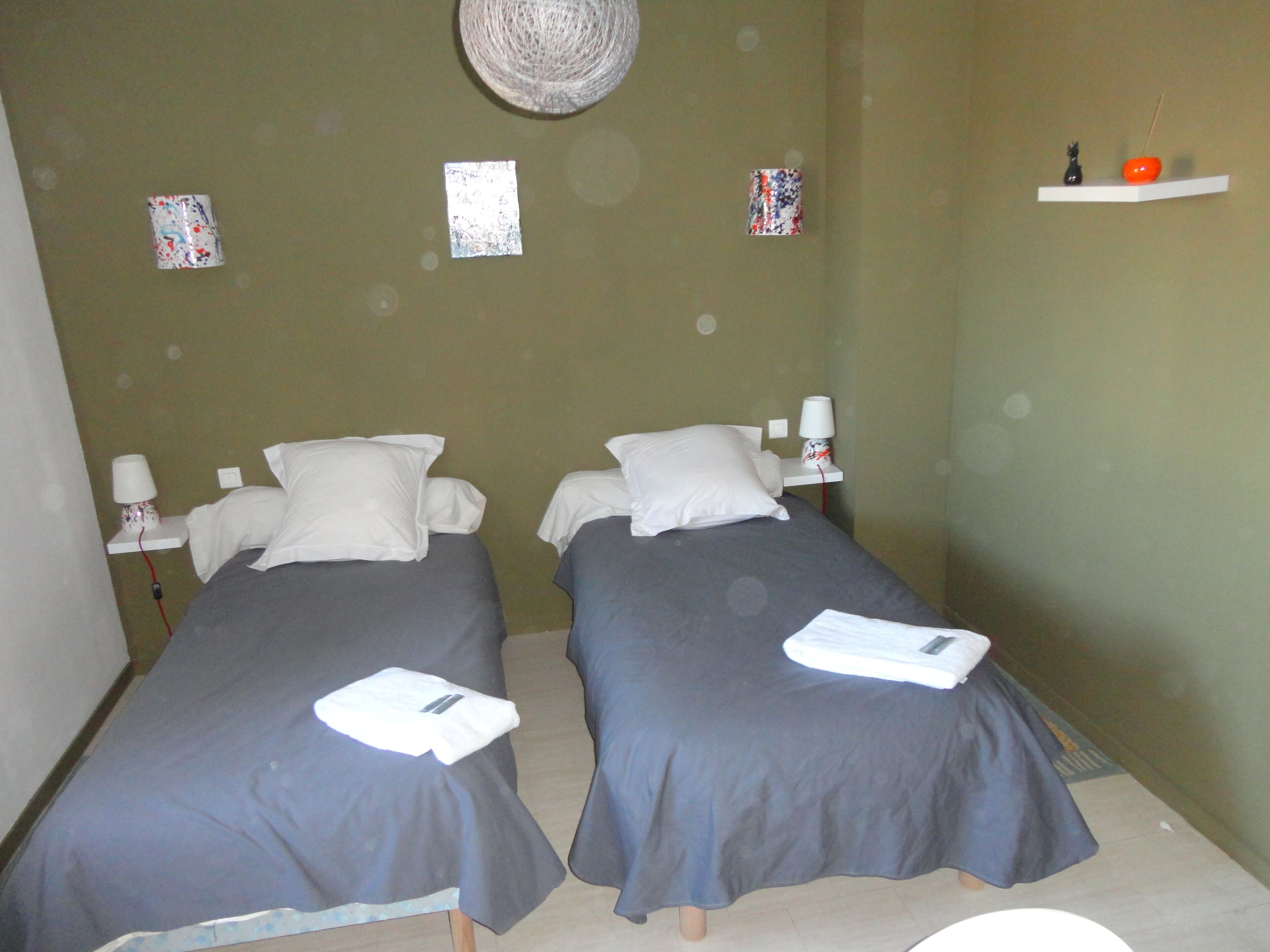 Habitación con dos camas, cada una con una almohada y una toalla doblada. Decoración en las paredes y una repisa con una figurita y una manzana.