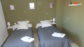 Habitación con dos camas, cada una con una almohada y una toalla doblada. Decoración en las paredes y una repisa con una figurita y una manzana.
