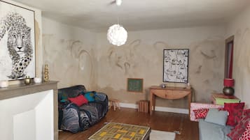 Un salon comprenant un canapé, une petite table, un luminaire suspendu et deux œuvres d’art murales.