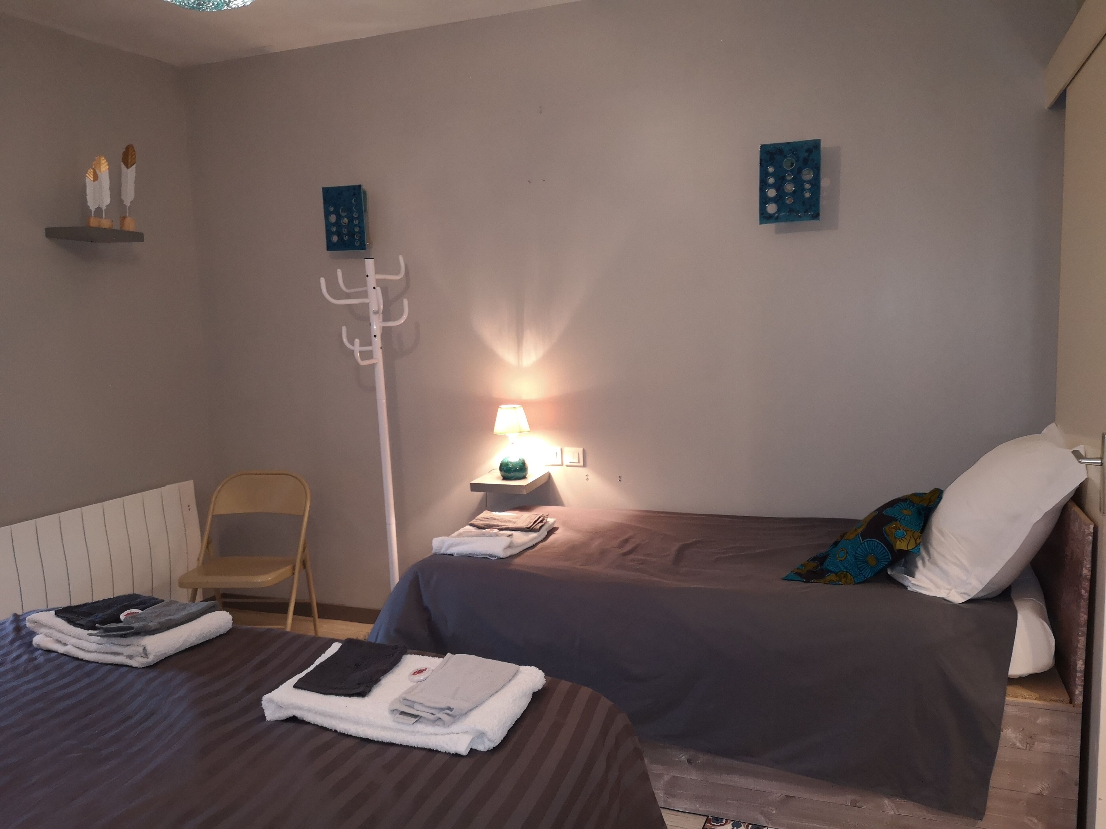 Een hotelkamer met een bed, een stoel, een nachtkastje met lamp en een wandplank met decoratieve objecten.