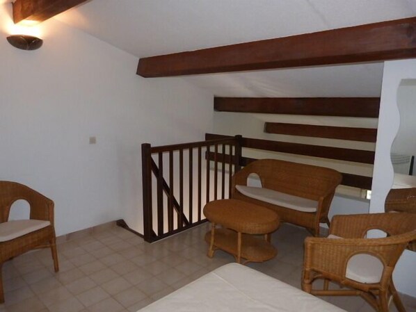 A room with a high ceiling, wooden beams, wicker furniture, and a white wall.