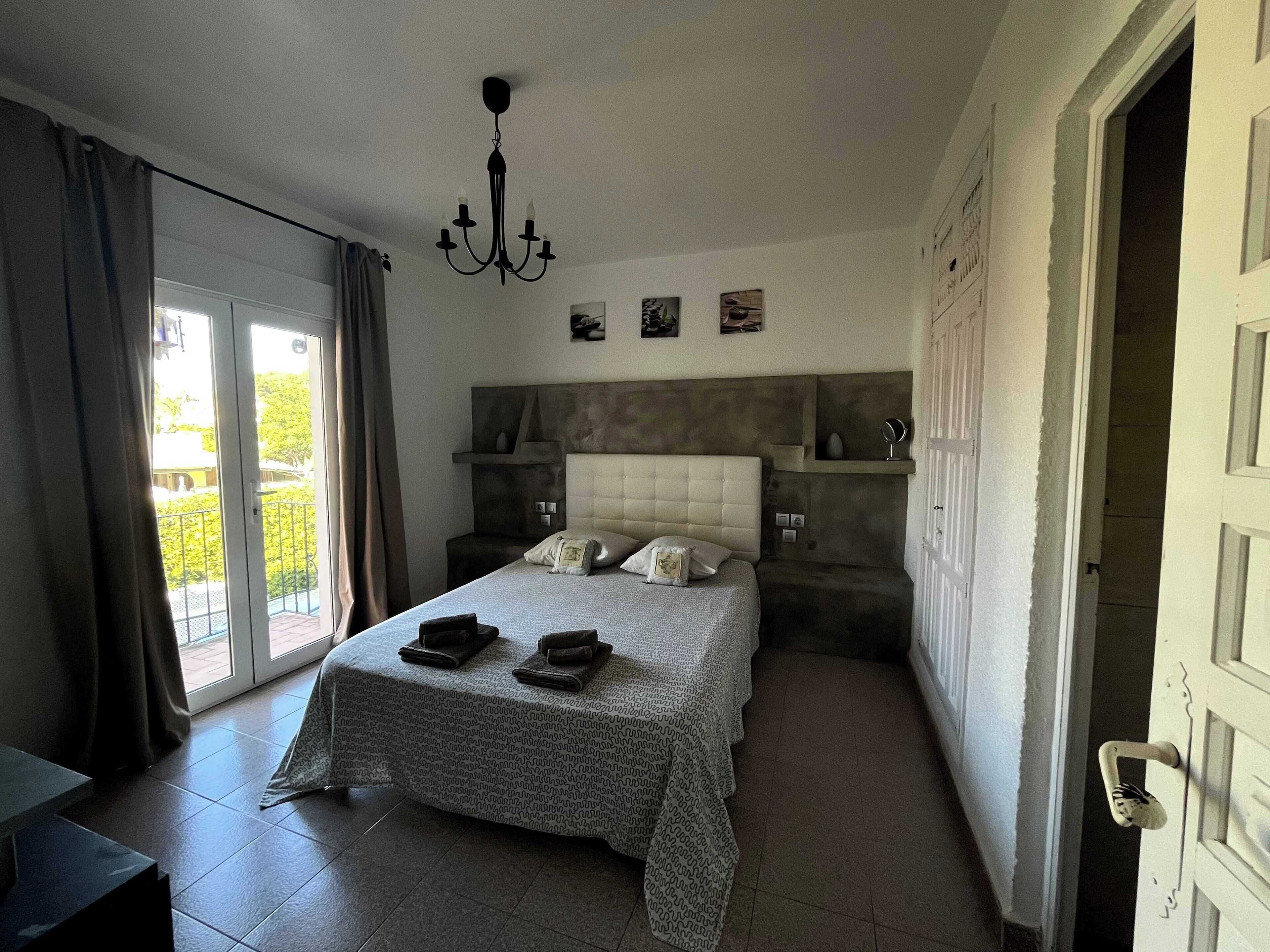 A bedroom with a large bed, a chandelier, a view through a sliding door, and a door handle.