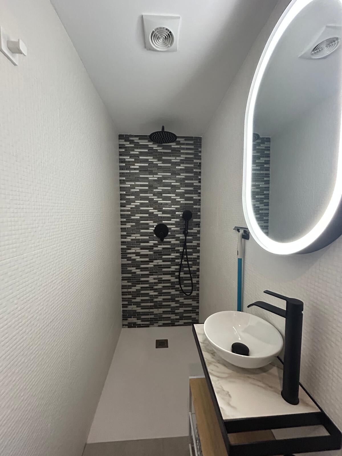 A modern bathroom with a white sink, black faucet, and a mirror with a round light.