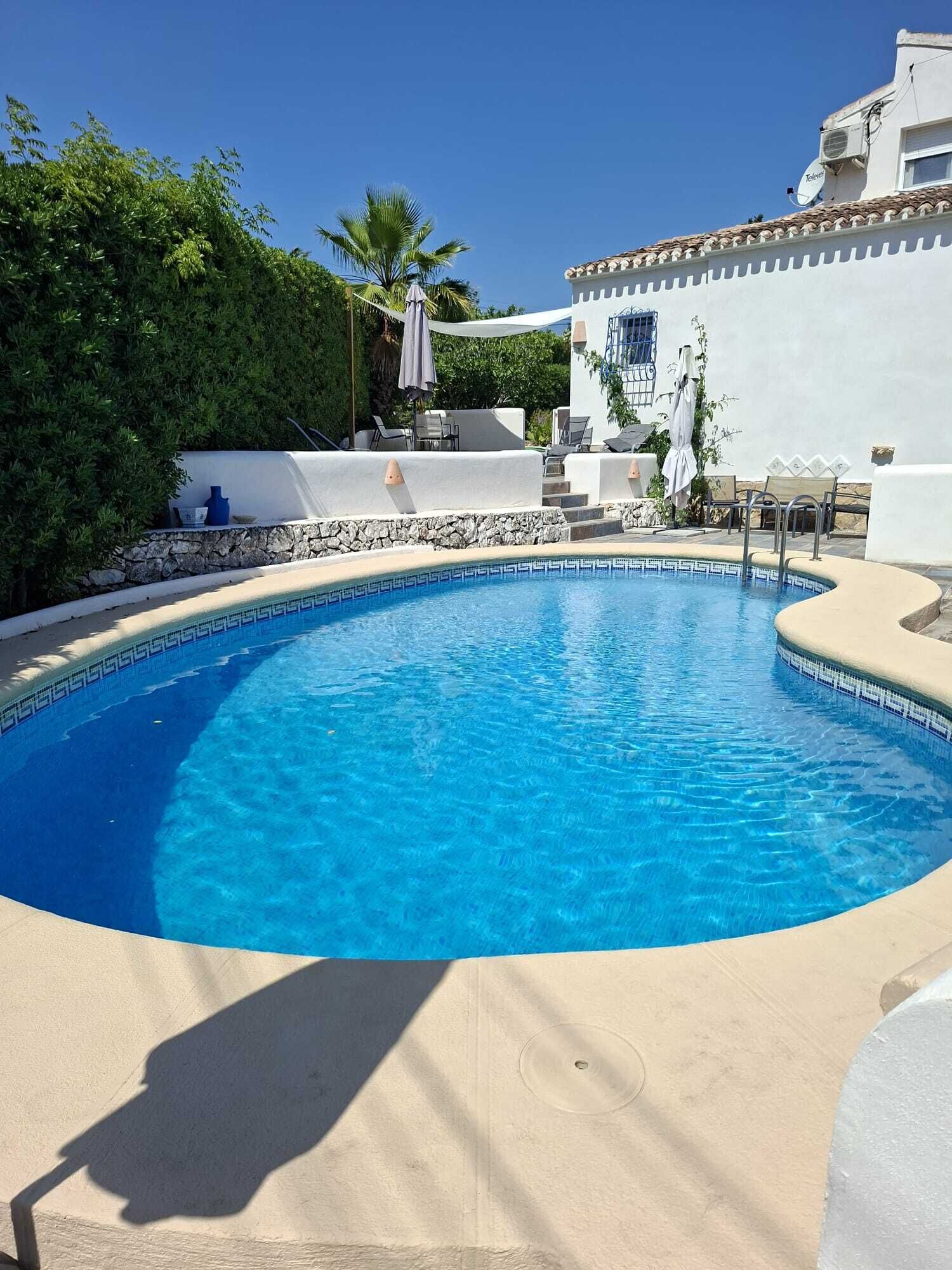 A swimming pool with a stone wall and lounge chairs.