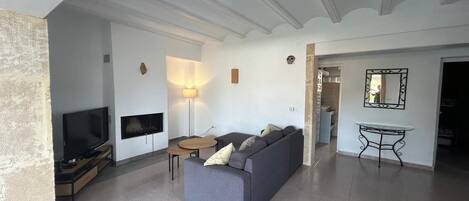 En moderne stue med en grå sofa, et fladskærms-tv, en pejs og et spiseområde med et lille bord og stole.