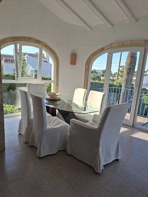 A dining area with a glass table, white chairs, and large arched windows. - Character villa for families in residential area with private pool. (JAVEA)