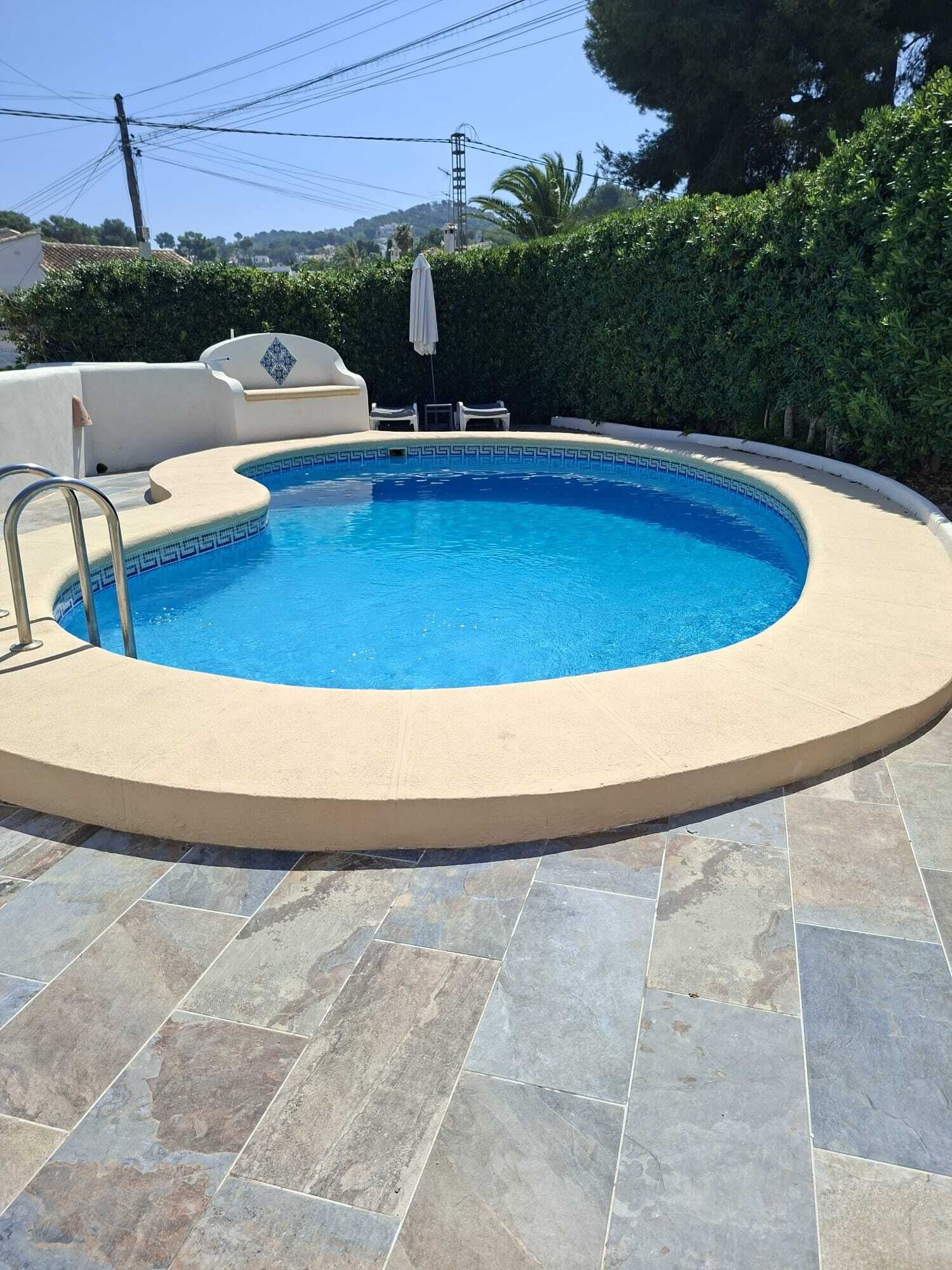 A circular swimming pool with a tiled deck, a lounge chair, and a small table.