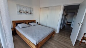 Un dormitorio con una cama de madera, una mesita de noche, una puerta blanca y un cuadro con barcos de vela en la pared.