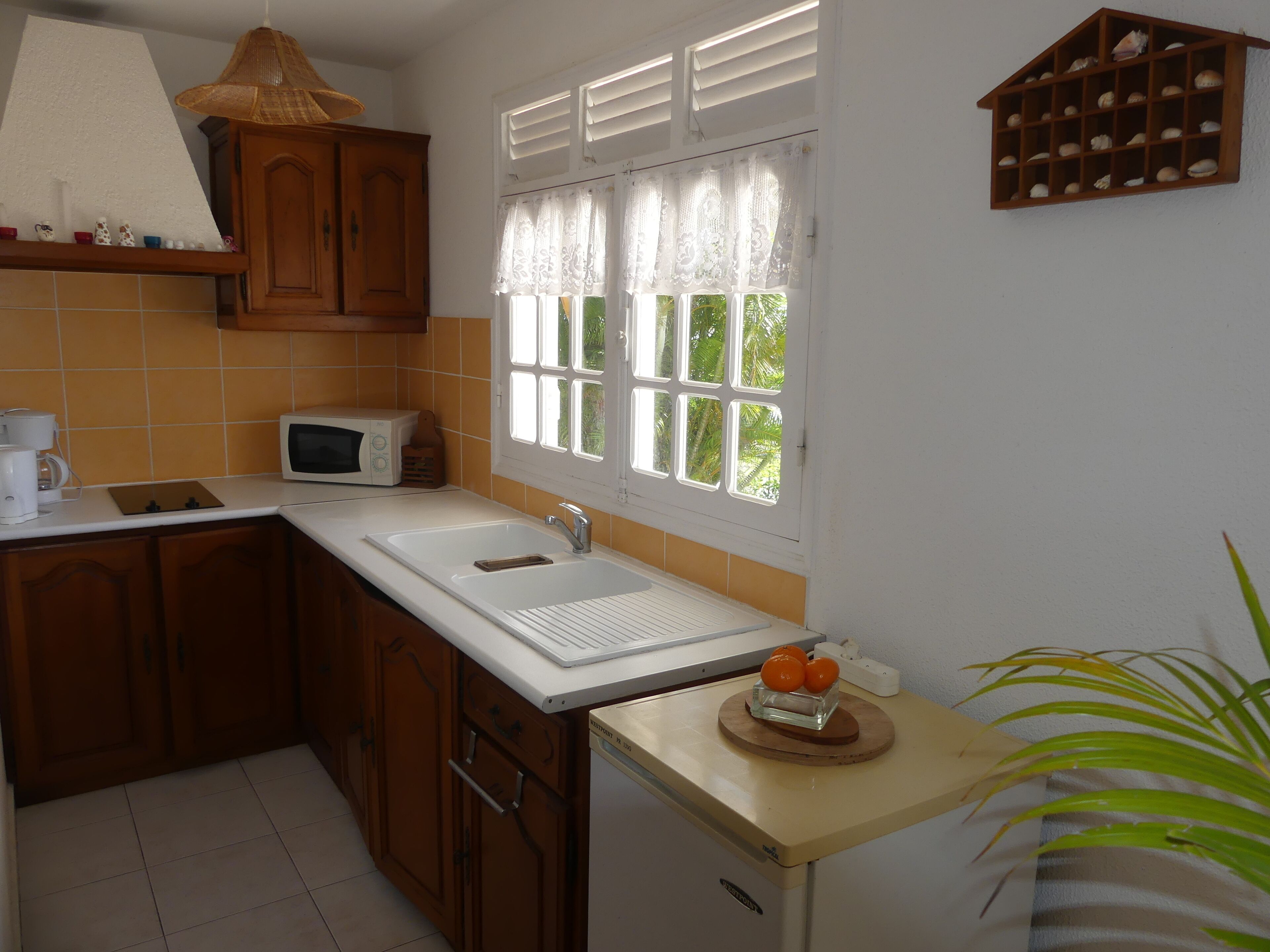 A kitchen with wooden cabinets, a microwave, a sink, and a window with white shutters.
