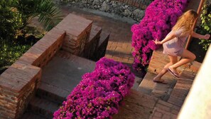 Une femme descend un escalier en briques, entourée de fleurs roses éclatantes.