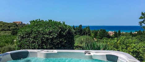 A hot tub with a clear view of the sea and a building in the background.