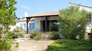 Une maison dotée d’un patio abrité, d’un jardin avec différentes espèces de plantes et d’un ciel dégagé.