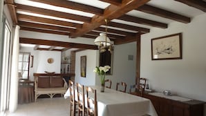 Un espace repas avec une longue table, des chaises en bois, un lustre et une cheminée.