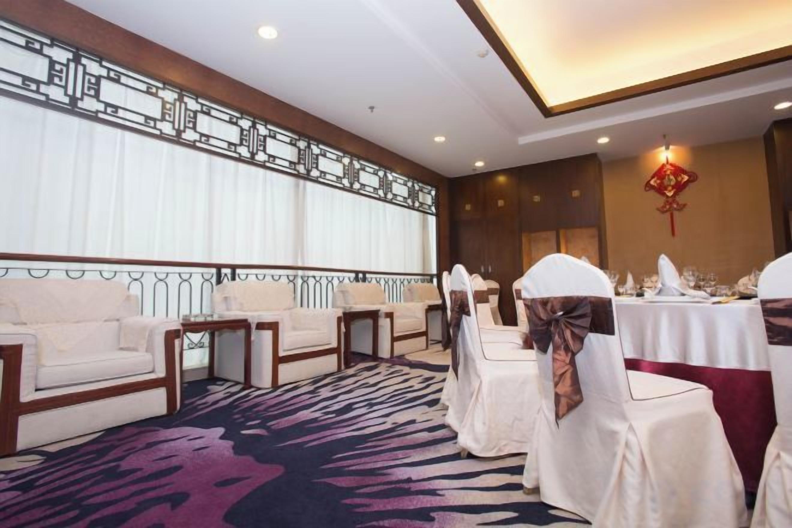 Un salón de conferencias con mesas redondas, sillas blancas y una alfombra estampada.