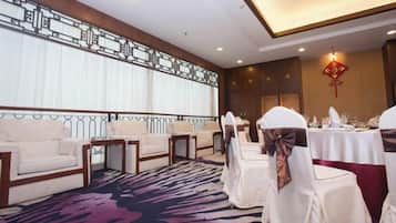 Un salón de conferencias con mesas redondas, sillas blancas y una alfombra estampada.