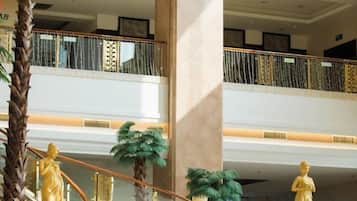 A multi-level interior with a central staircase, palm trees, and golden statues.
