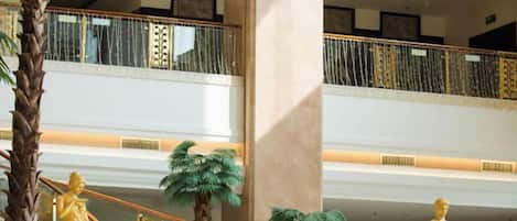 A multi-level interior with a central staircase, palm trees, and golden statues.