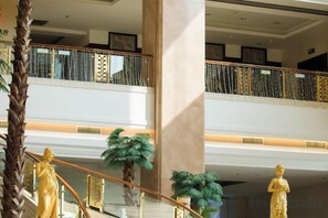 A multi-level interior with a central staircase, palm trees, and golden statues. - Perfect International Hotel (Qidong)