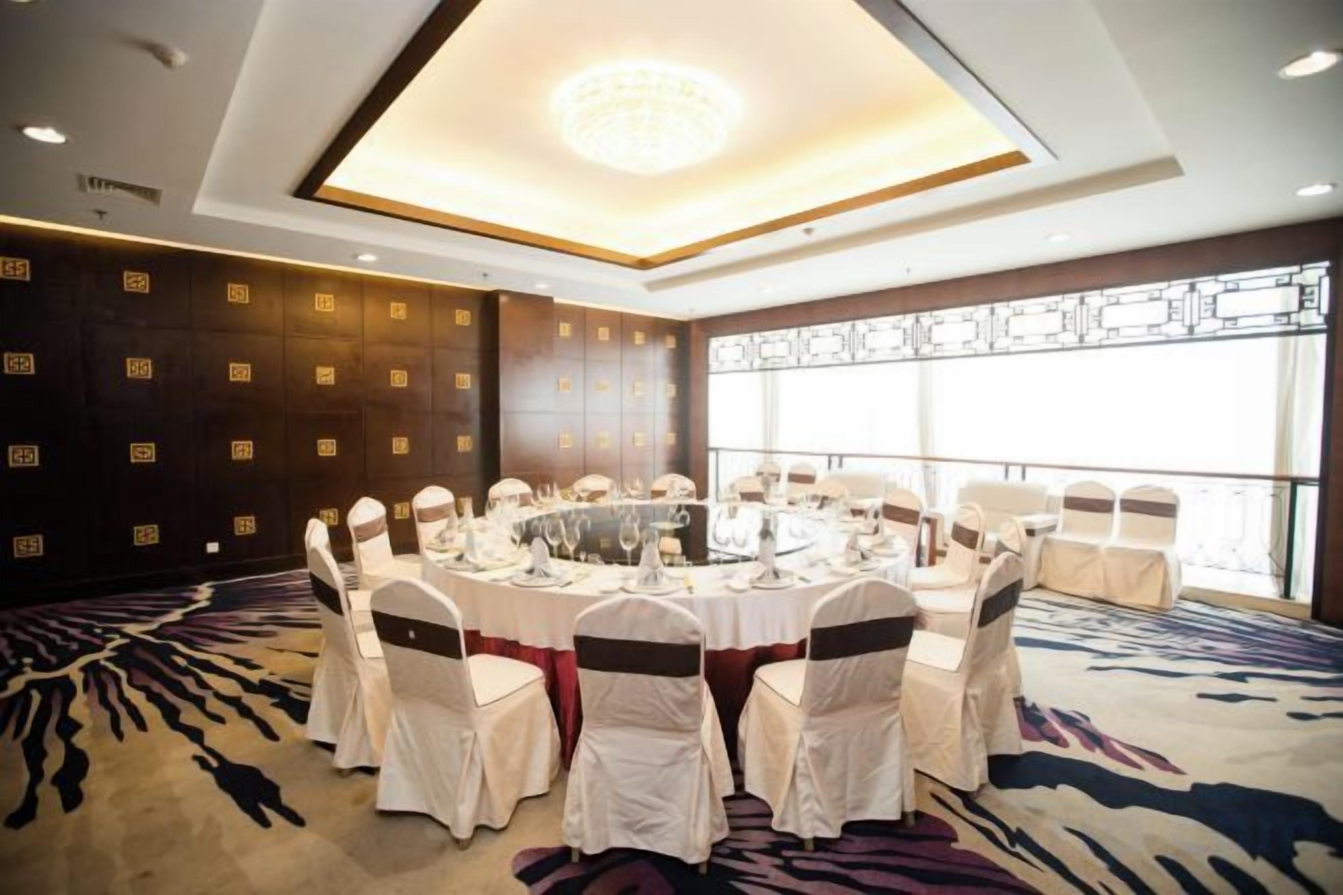 A conference room with a round table, white chairs with sashes, and a patterned carpet.